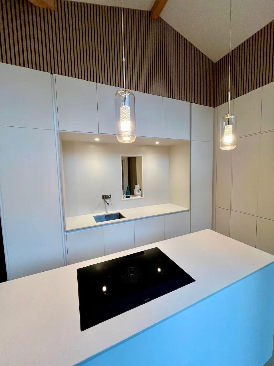Cuisine sur mesure blanche, îlot avec plaque, mur tasseaux bois