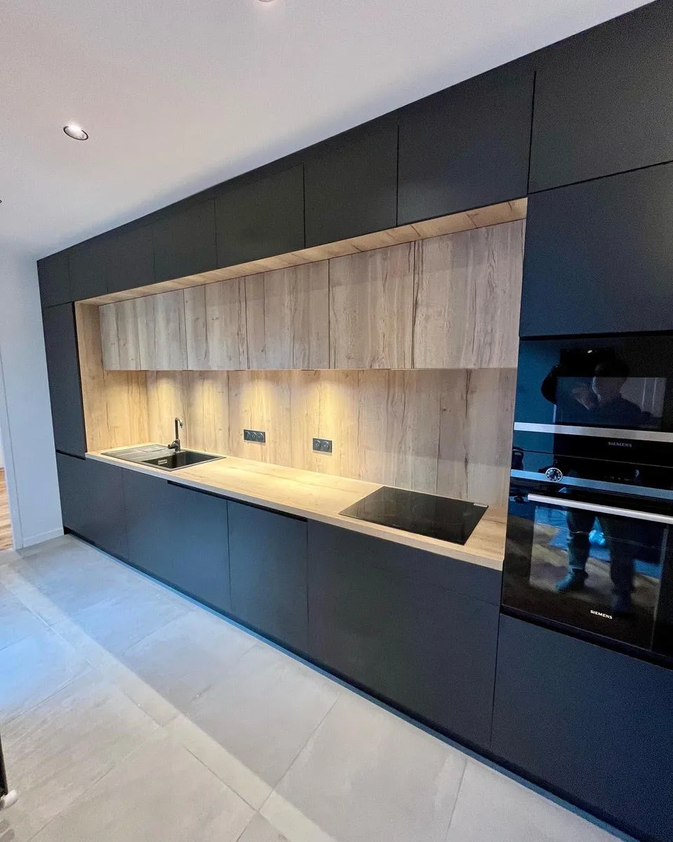 Cuisine sur mesure noire mate, crédence et niche en bois clair rétroéclairée, four et plaque Siemens, réalisée par Technibois Agencement